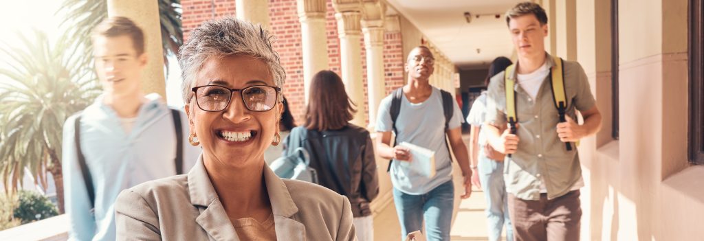 Image of a female high school teacher smiling as students walk behind her