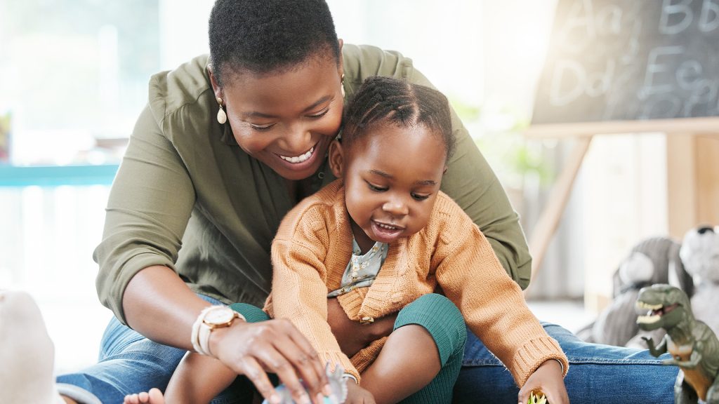 Black woman, teacher and girl with playing in kindergarten with toys for fun, education and child development. People, educator and happy on floor at school with support, care and help in day care