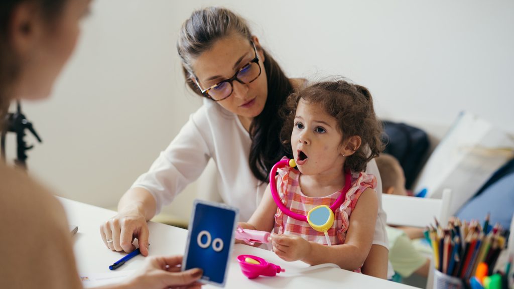 mother with her child in kindergarten, learning how to correct p